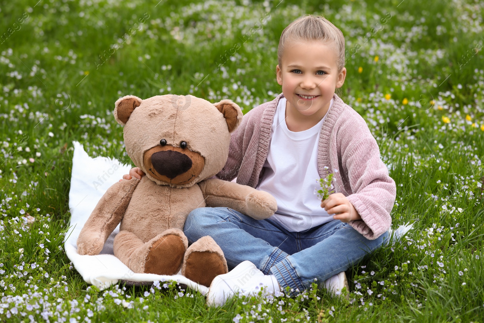 Photo of Little girl with teddy bear on plaid outdoors