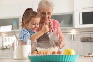 Photo of Cute girl and her grandmother cooking in kitchen