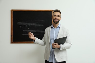 Teacher near black chalkboard with music notes in classroom