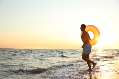 Young man with inflatable ring on beach