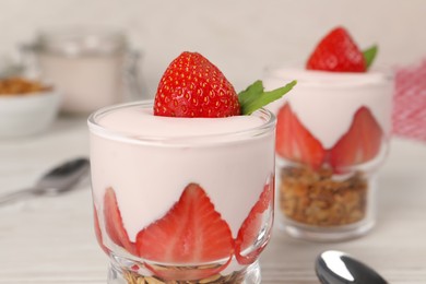 Glasses of tasty yogurt with muesli and strawberries served on white table, closeup