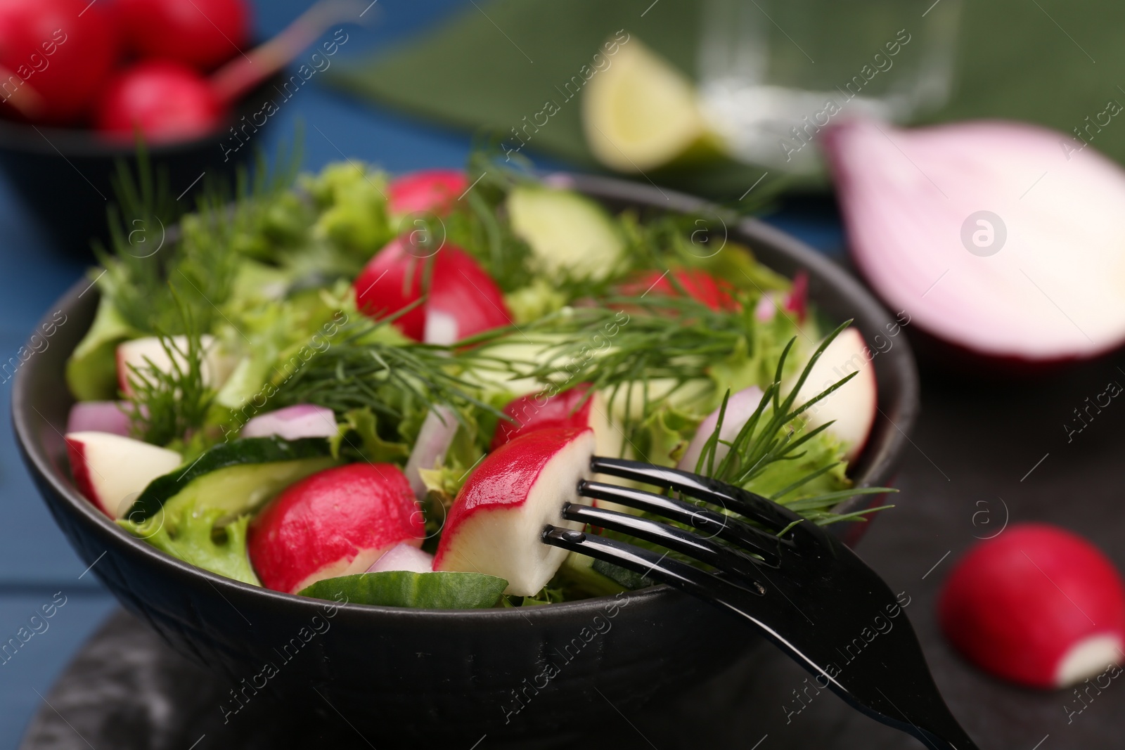 Photo of Tasty salad with radish in bowl and fork on blue table, closeup