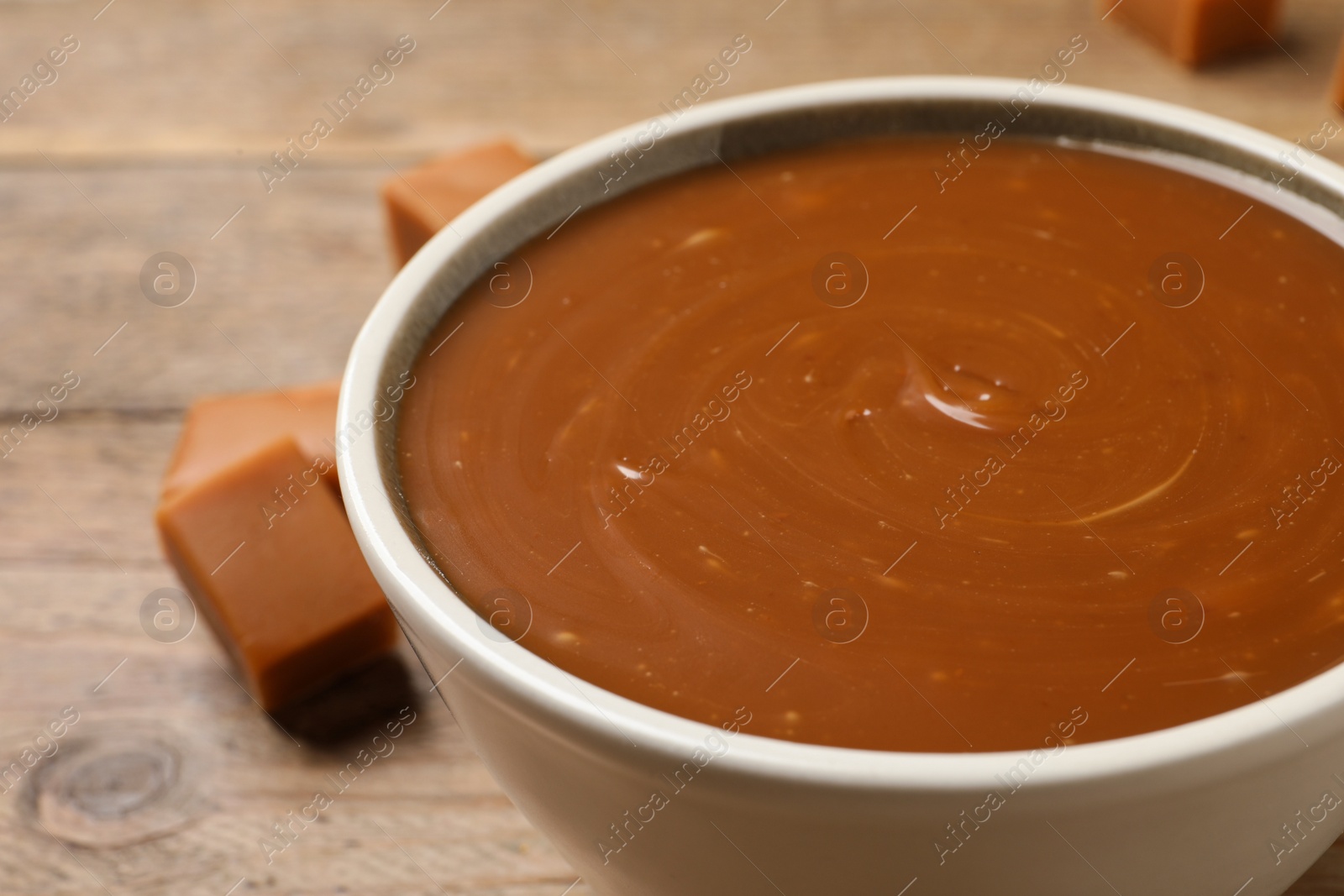 Photo of Yummy salted caramel in bowl on wooden table, closeup
