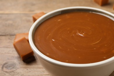 Yummy salted caramel in bowl on wooden table, closeup