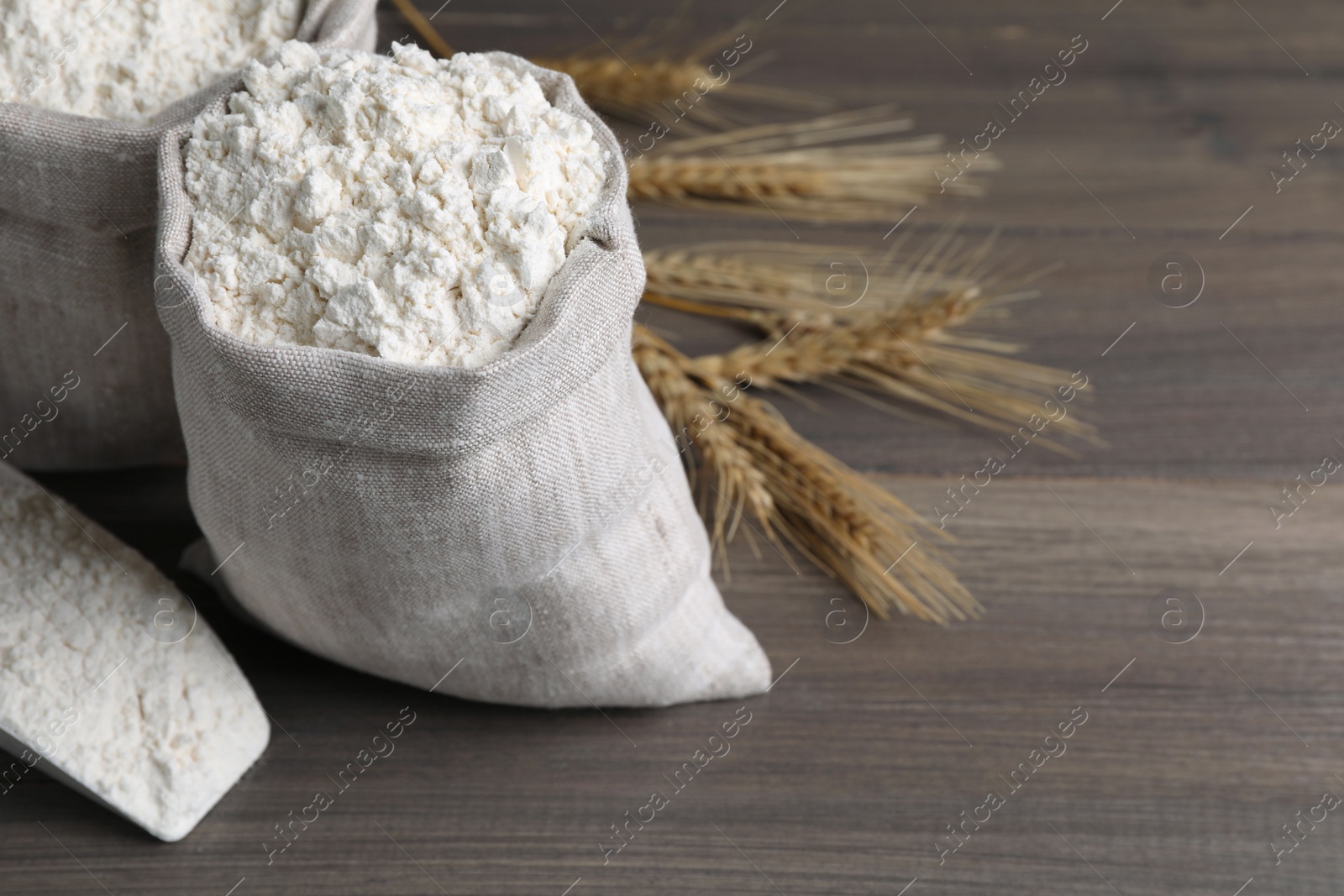 Photo of Sacks with flour and wheat spikes on wooden background, space for text