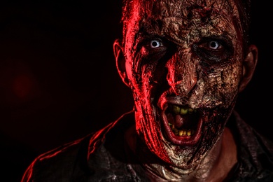 Photo of Scary zombie on dark background, closeup. Halloween monster