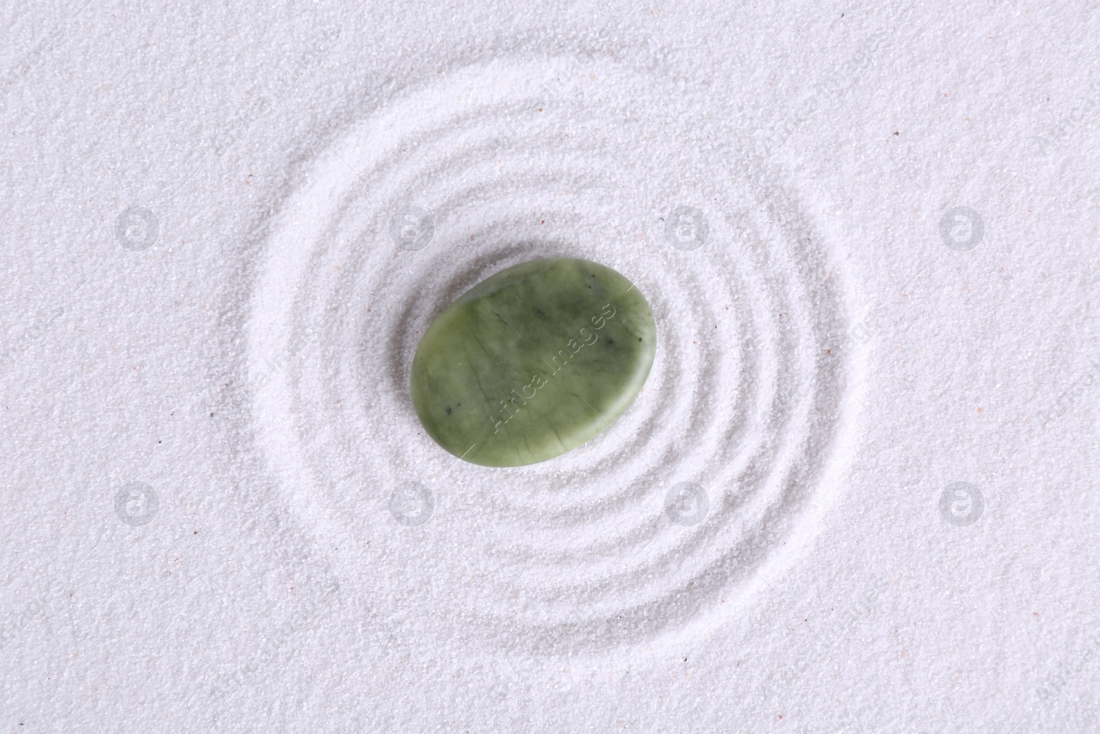 Photo of Zen garden stone on white sand with pattern, top view