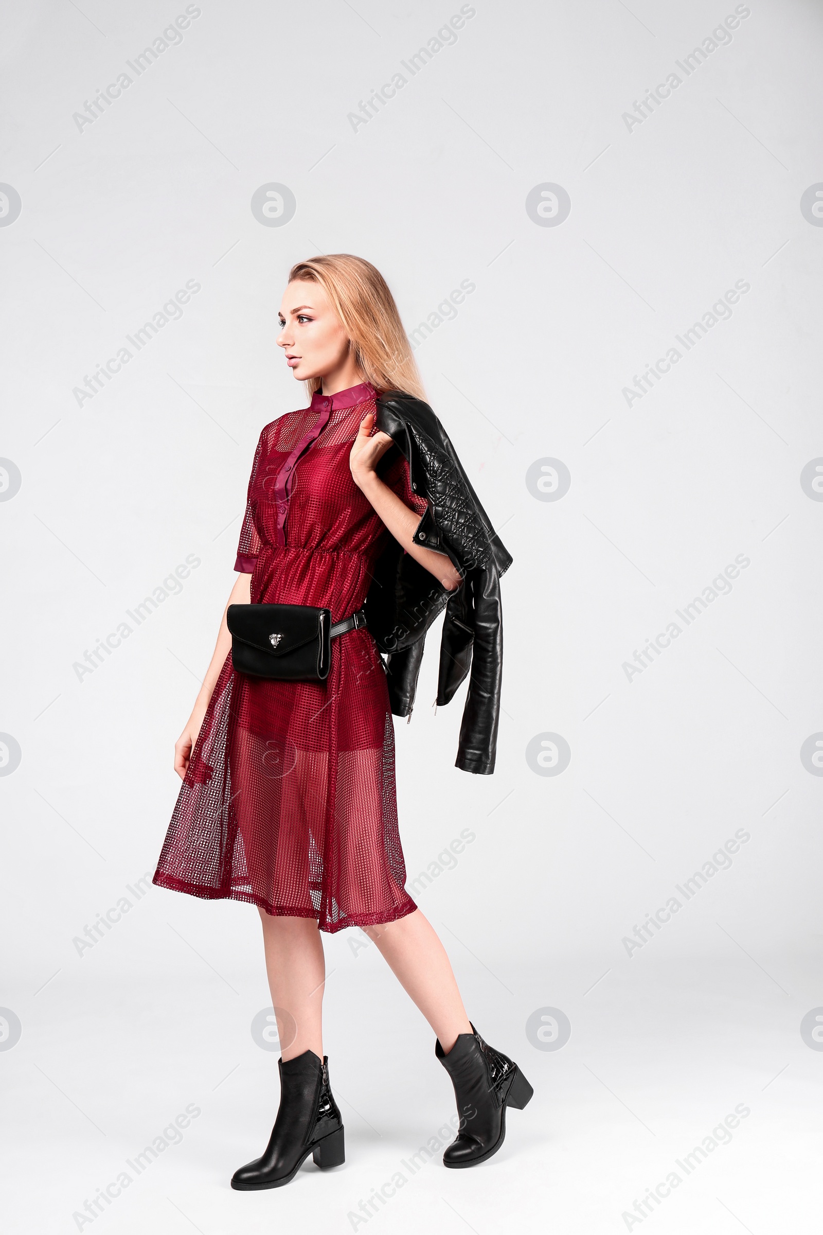 Photo of Young stylish woman in trendy shoes with bum bag on light background