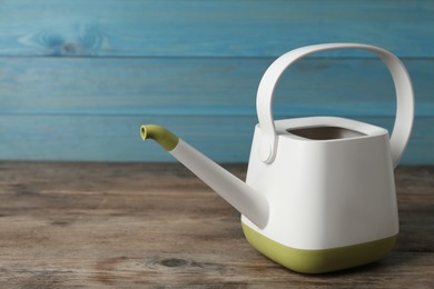 Modern watering can on wooden table, space for text