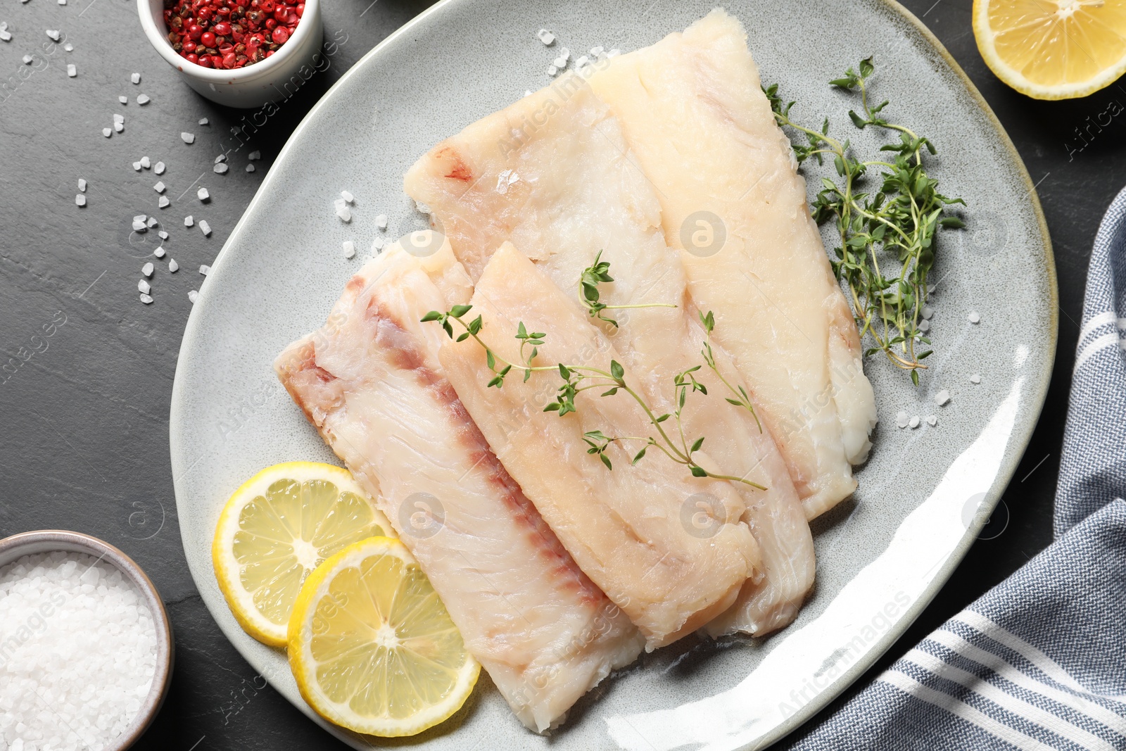 Photo of Raw cod fish, microgreens, lemon and spices on dark table, flat lay