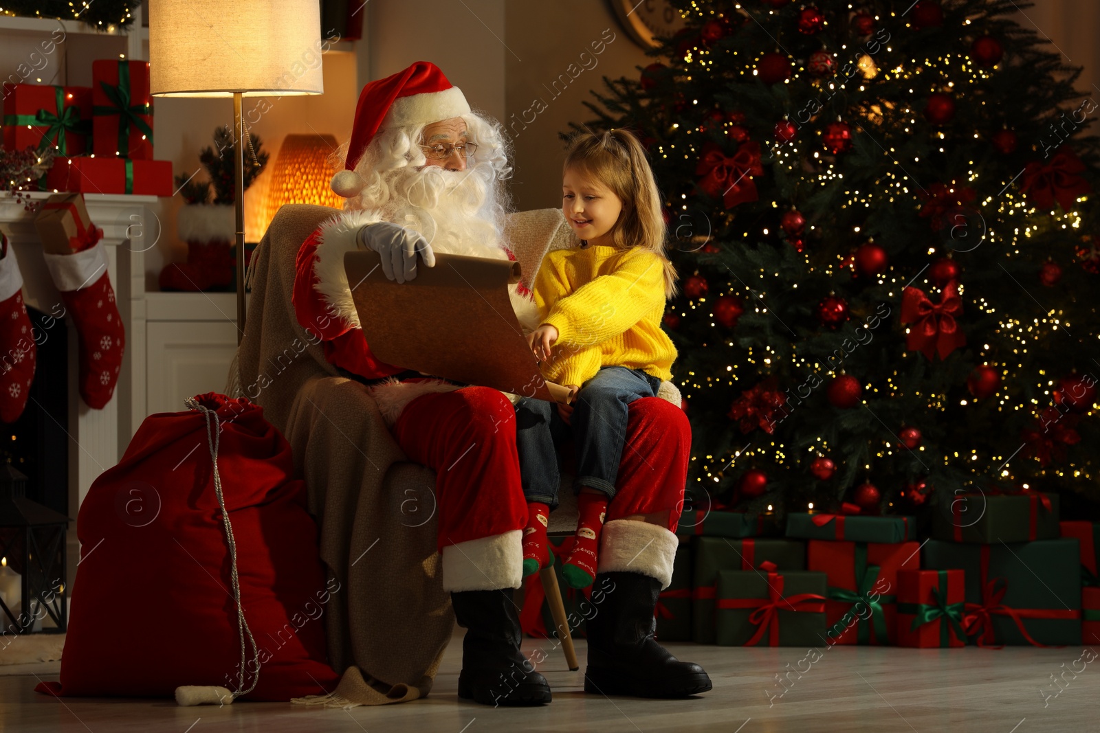 Photo of Merry Christmas. Santa Claus with little girl reading her letter at home
