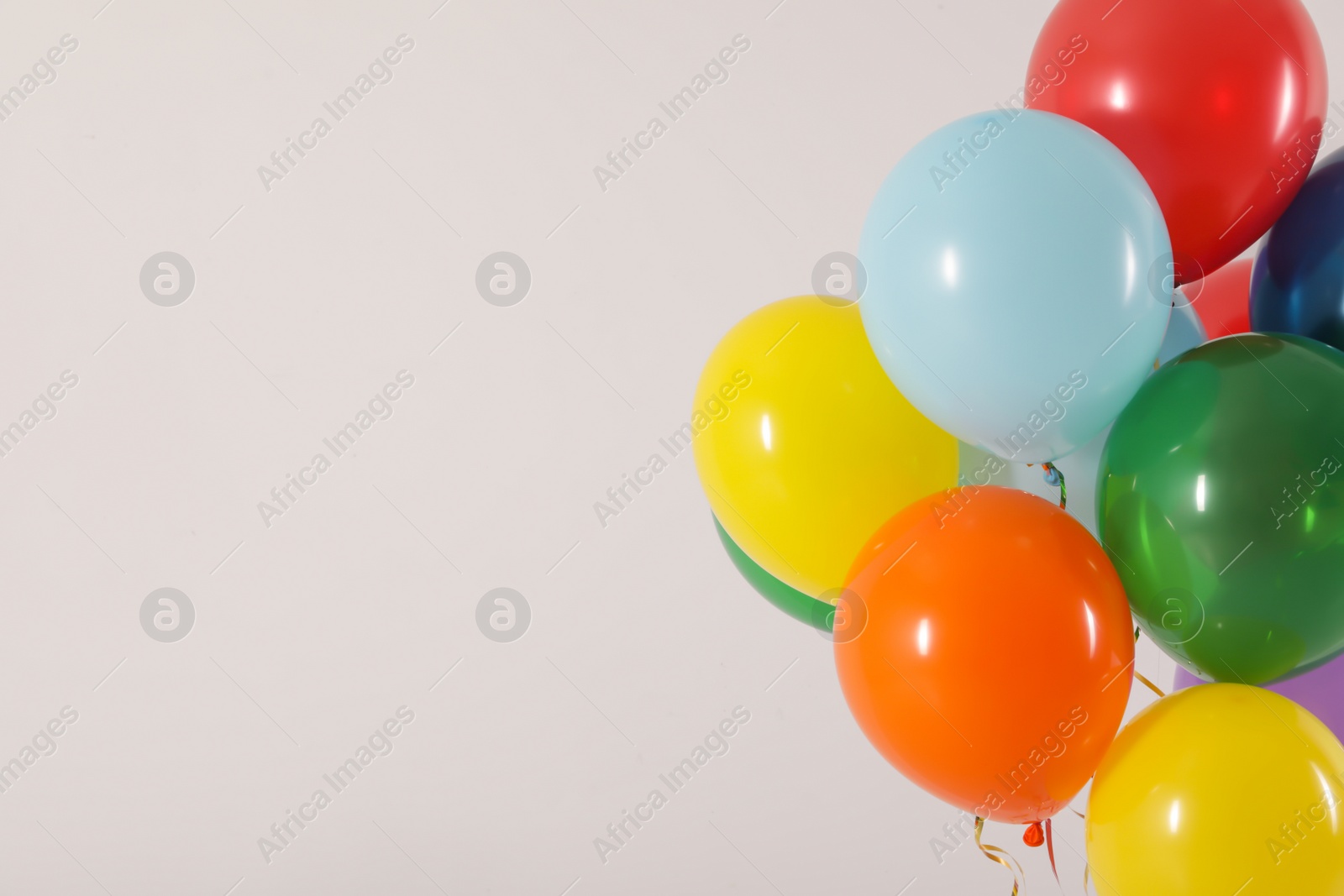 Photo of Bunch of bright balloons on light background, space for text. Celebration time