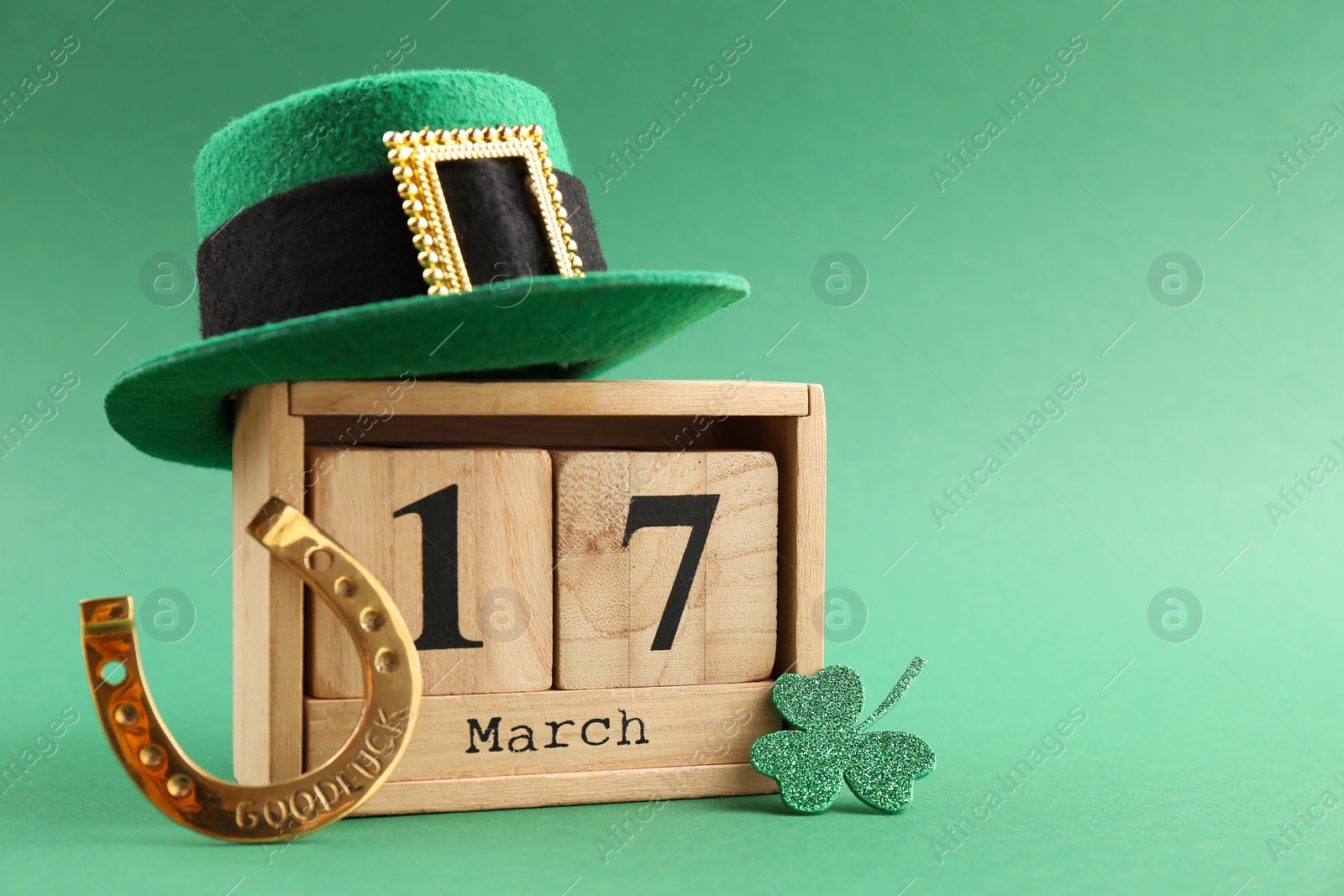 Photo of St. Patrick's day - 17th of March. Wooden block calendar, leprechaun hat, golden horseshoe and decorative clover leaf on green background. Space for text