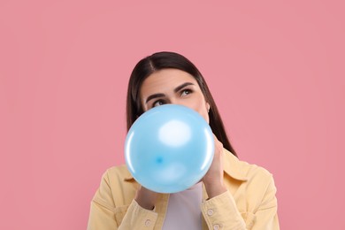 Woman inflating light blue balloon on pink background