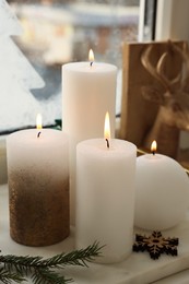 Beautiful burning candles with Christmas decor on windowsill indoors