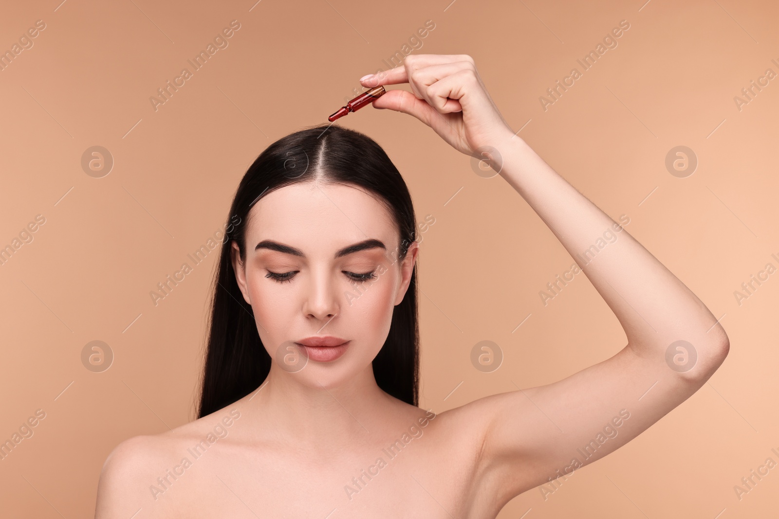 Photo of Beautiful young woman using ampoule for hair treatment on beige background