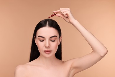 Photo of Beautiful young woman using ampoule for hair treatment on beige background