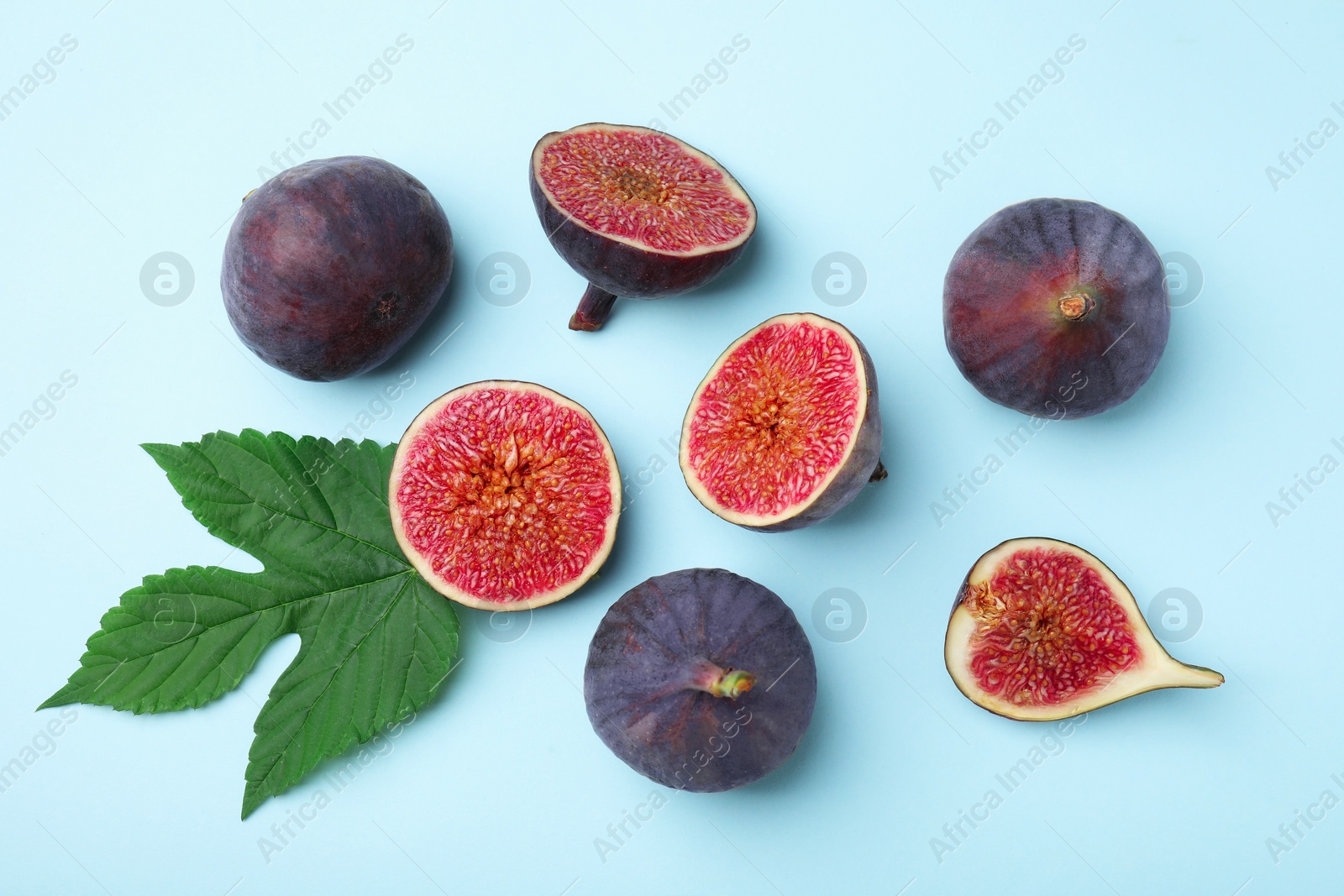 Photo of Fresh ripe figs with green leaf on light blue background, flat lay