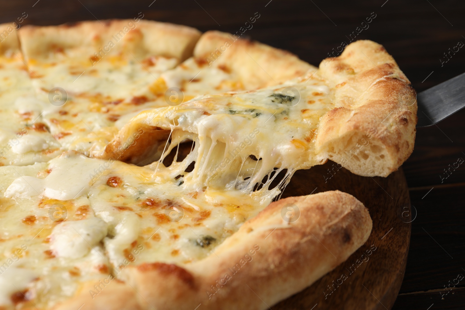 Photo of Taking piece of delicious cheese pizza at wooden table, closeup