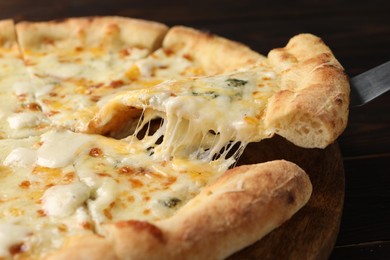 Taking piece of delicious cheese pizza at wooden table, closeup