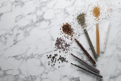 Photo of Glass tubes with different spices on white marble table, flat lay. Space for text