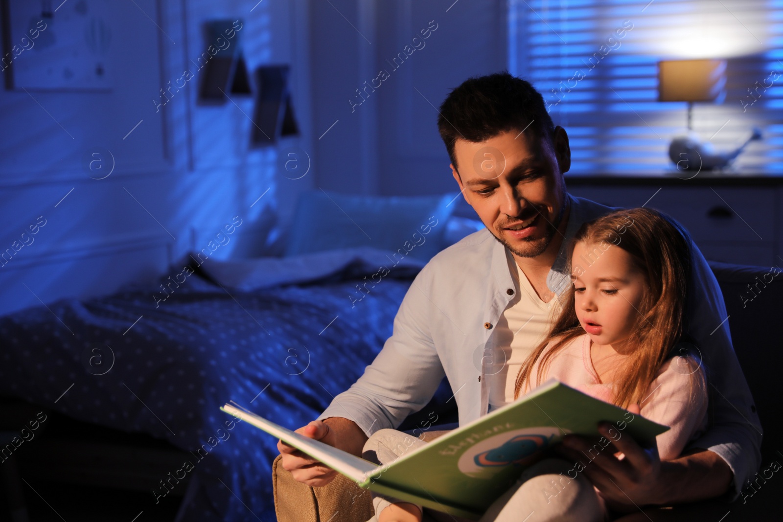 Photo of Father reading bedtime story to his daughter at home