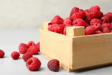 Photo of Wooden crate with delicious ripe raspberries on table against light background, closeup. Space for text