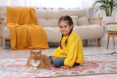 Photo of Smiling little girl and cute ginger cat on carpet at home