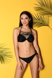 Beautiful young woman in black bikini and tropical leaves on yellow background