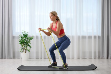 Athletic woman doing exercise with fitness elastic band on mat at home