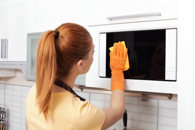 Woman cleaning microwave oven with rag in kitchen