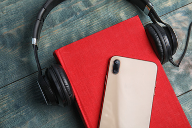 Photo of Book, modern headphones and smartphone on blue wooden table, closeup