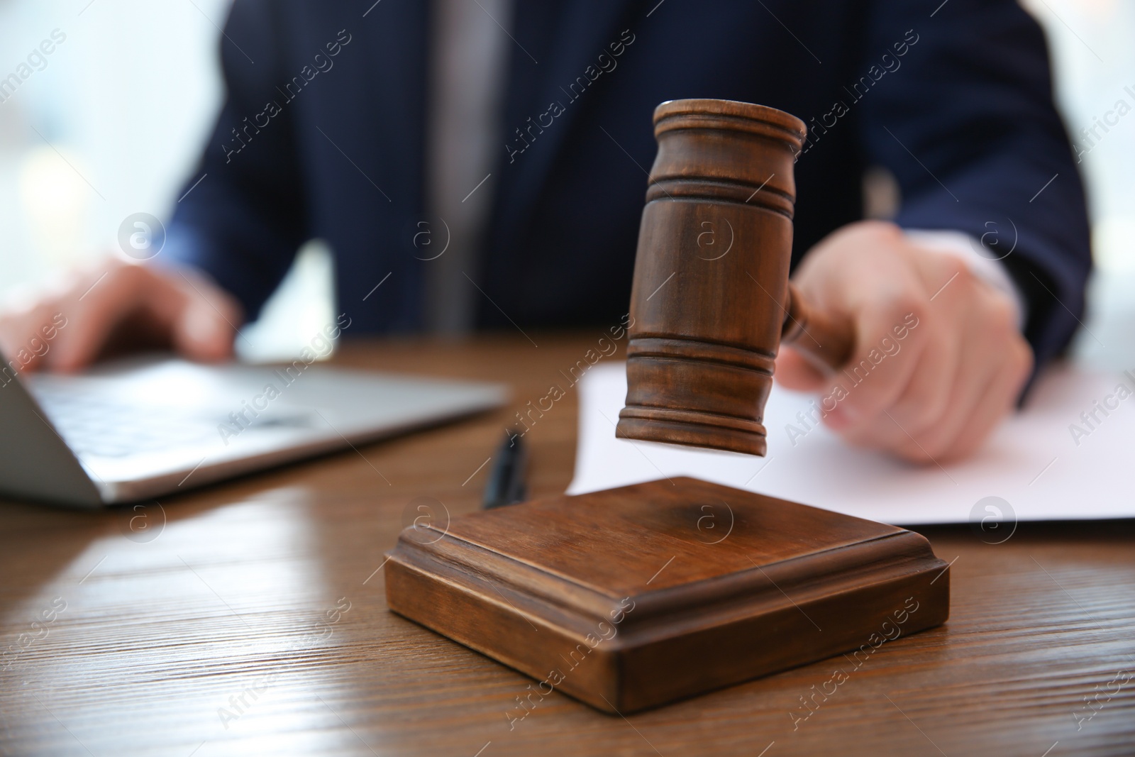 Photo of Judge with gavel at table in courtroom, closeup. Law and justice concept