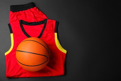 Photo of Basketball uniform and ball on black background, top view. Space for text