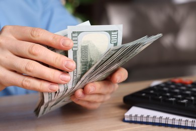 Photo of Money exchange. Woman counting dollar banknotes at wooden table, closeup