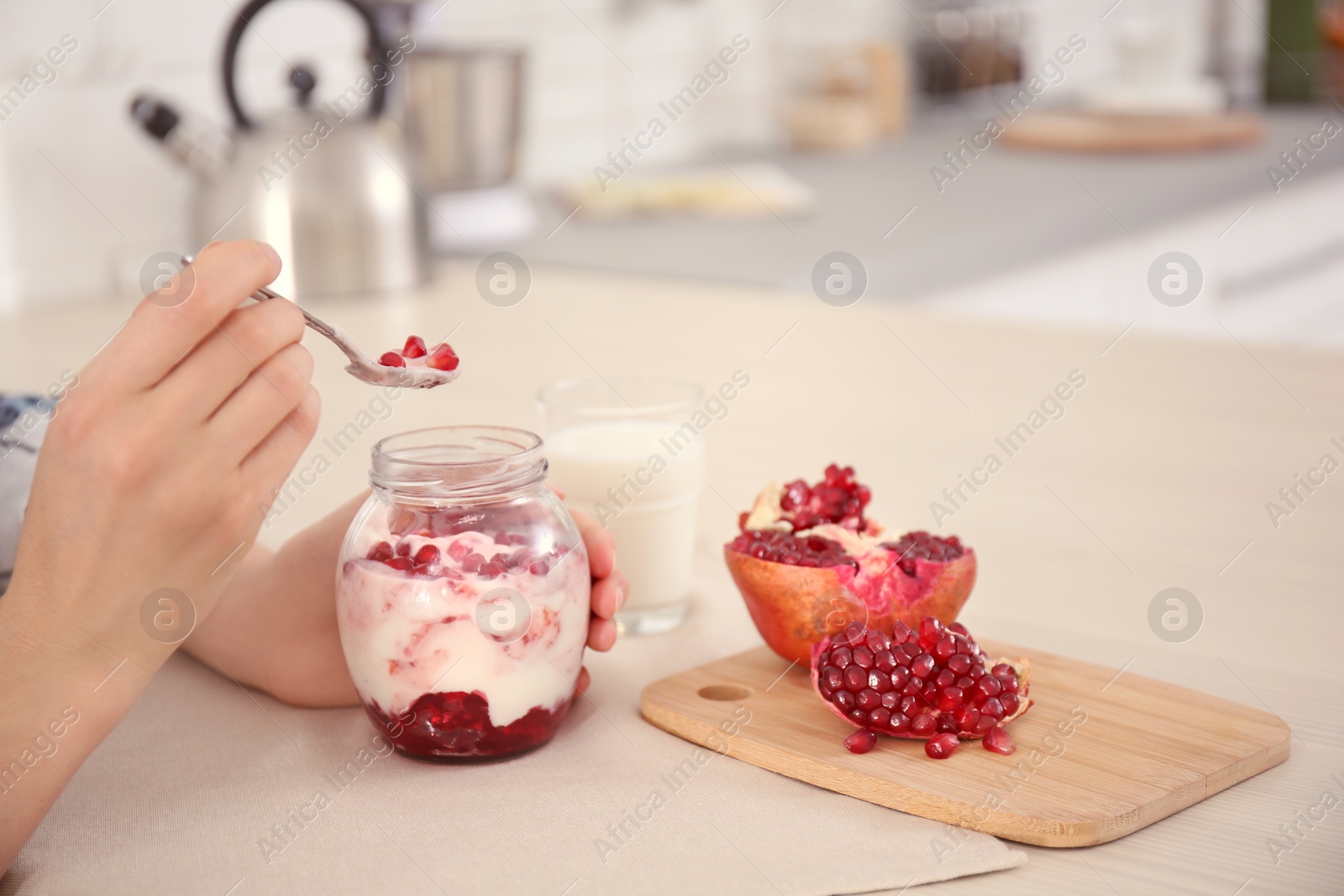 Photo of Young woman eating tasty yogurt with pomegranate seeds at table