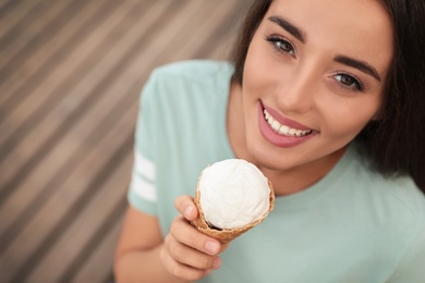 Happy young woman with delicious ice cream in waffle cone outdoors
