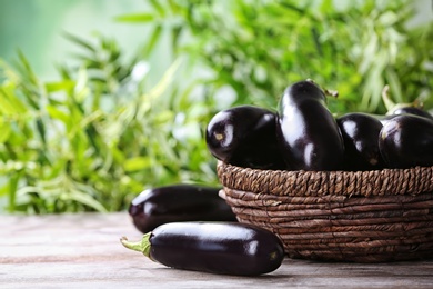 Photo of Bowl with ripe eggplants on table against blurred background