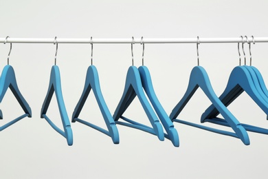 Photo of Empty clothes hangers on metal rail against light background