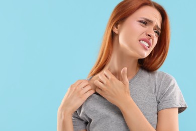 Photo of Suffering from allergy. Young woman scratching her neck on light blue background, space for text