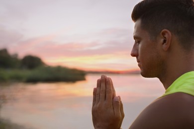 Photo of Man meditating near river at sunset. Space for text