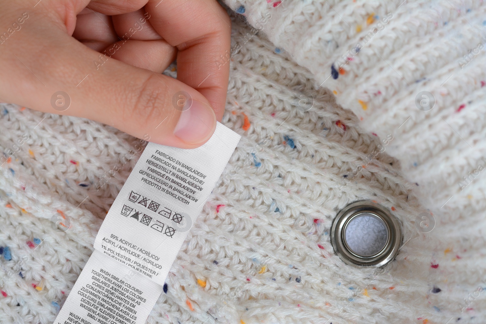 Photo of Woman holding white clothing label on beige warm sweater, closeup