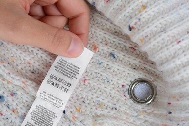 Woman holding white clothing label on beige warm sweater, closeup