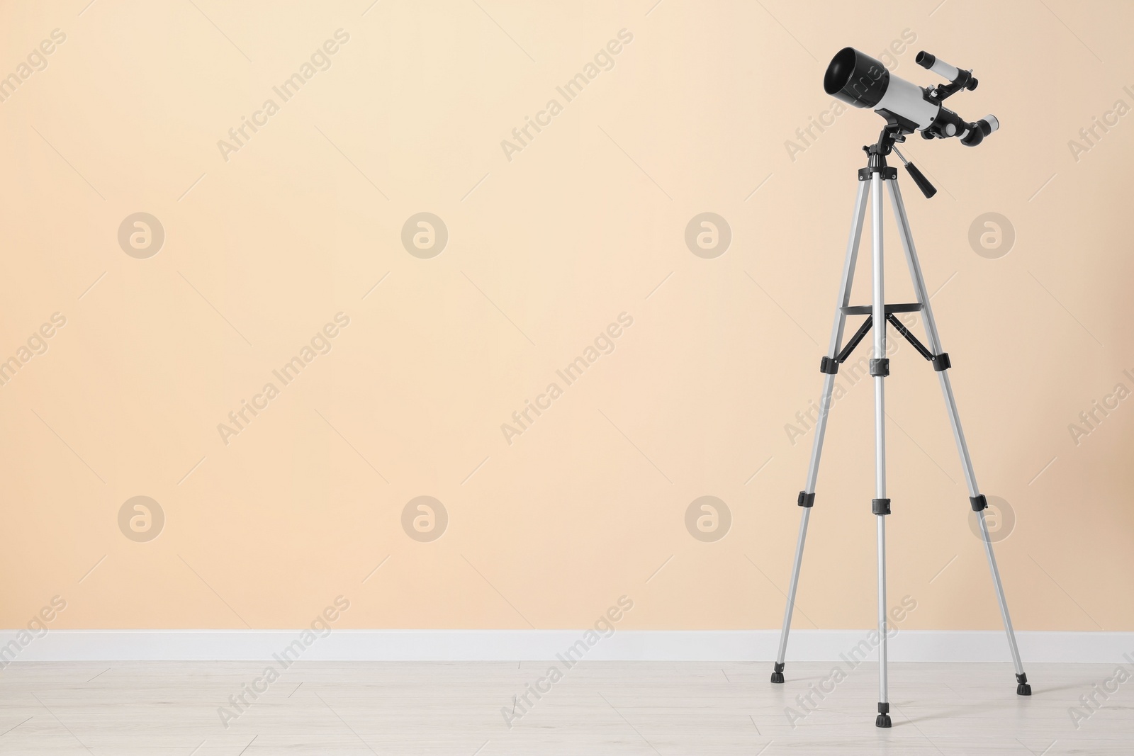 Photo of Tripod with modern telescope near beige wall. Space for text