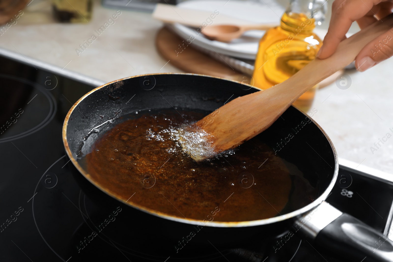 Photo of Woman with wooden spatula and frying pan of used cooking oil near stove, closeup