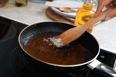 Woman with wooden spatula and frying pan of used cooking oil near stove, closeup