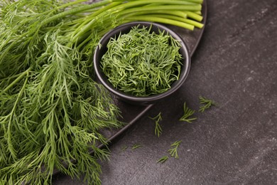 Photo of Sprigs of fresh dill and bowl with cut one on dark textured table, closeup