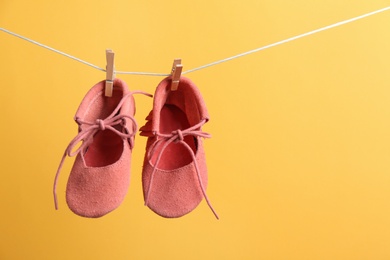 Photo of Cute small shoes hanging on washing line against color background, space for text. Baby accessories