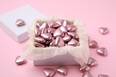 Box and delicious heart shaped candies on pink background
