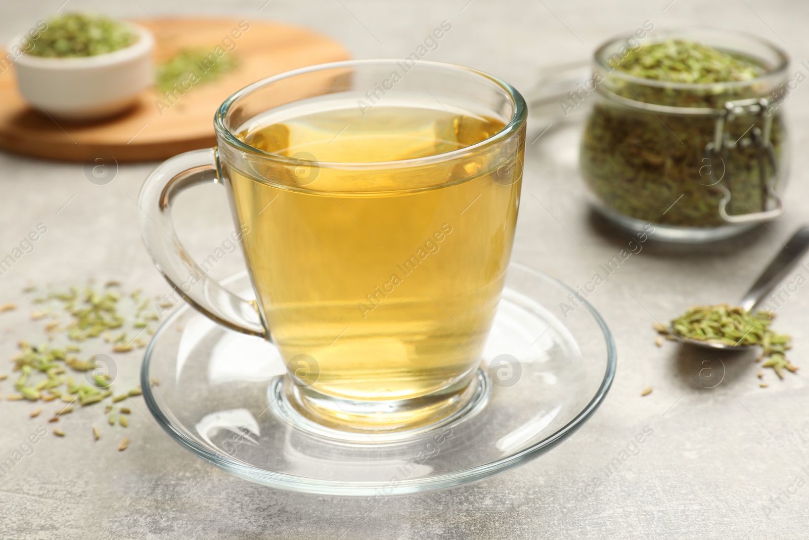 Photo of Aromatic fennel tea and seeds on light grey table, closeup